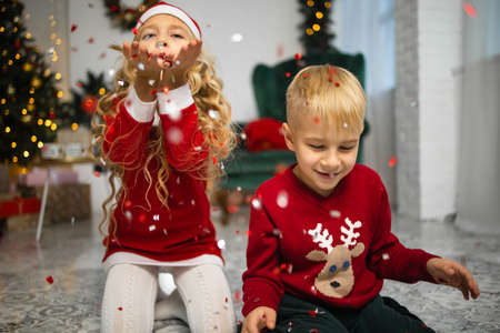 Little kids in christmas costume having fun beside a decorated christmas tree. Two kids playing with...