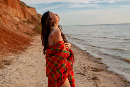 A asian girl stands near rocks overlooking the ocean with a blanketの写真素材