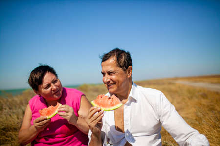Senior couple eatting watermelon relaxing by the sea on sunny summer dayの写真素材