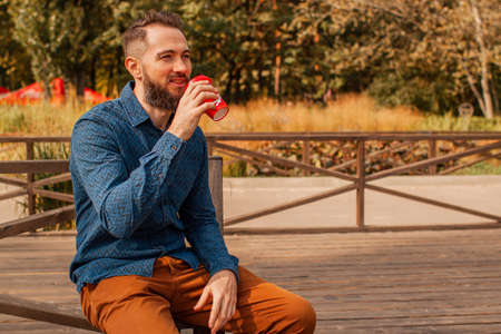 handsome middle-aged bearded man with paper cup of morning coffee walking in autumn park.の写真素材