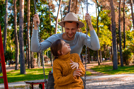Happy family. Father and daughter on a swing in autumn parkの写真素材
