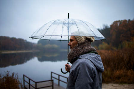 man with umbrella standing on lake pier in rainy day