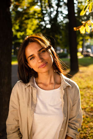 Portrait of beautiful american woman smiling and looking away at park during sunset. Outdoor portrait of a smiling girl. Happy cheerful girl laughing at parkの写真素材