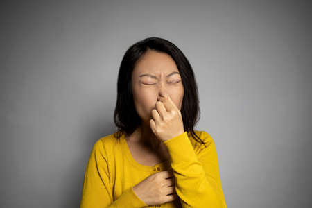 Smells bad, awful odor. Female gesture smells bad. Headshot woman pinches nose with fingers hands looks with disgust something stinks bad smell situation. Human face expression body language reactionの写真素材