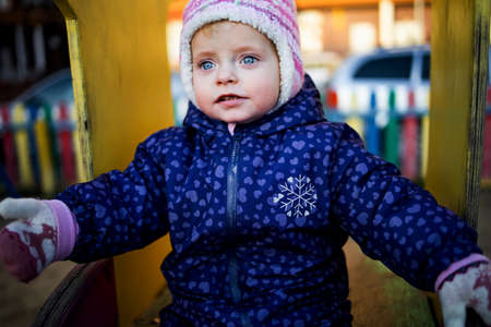 Little child girl, sitting at the playground in winter in cold weather.
