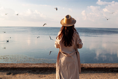 Young woman feeds seagulls at winter sea beach. Amazing coastline scene with girl. Concept of freedom, travel, flying. Lifestyle moment.の写真素材