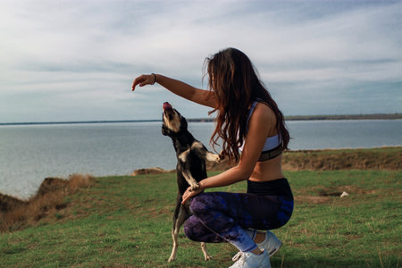 Girl with a dog play in the mountains. Woman with her dog sitting on a cliff near sea.の写真素材