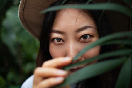 Young asian woman's face surrounded by tropical leaves. Closeup portrait of magnificent lady with natural nude makeup, perfect skin. Natural cosmetic, wellness, purity, skincare, beauty conceptの写真素材