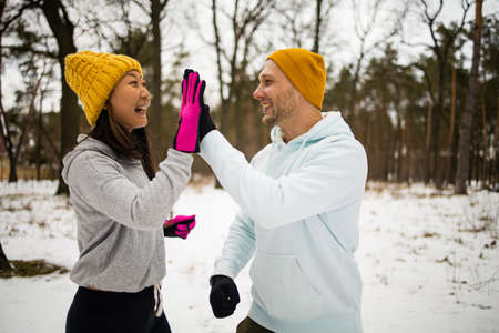 Fitness mixed race couple winter morning exercises on a snowy forest.