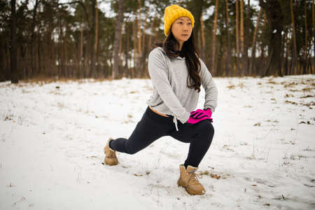 Beautiful young asian woman preparing for training. Snowy forest morning fitness.