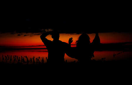 silhouettes of lovers couple hugging, kissing, touching, eye contact at sunset, sunrise against the backdrop of the sea, sun, clouds in fiery red, orange colorsの写真素材