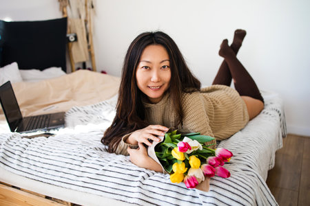 Beautiful asian woman with bouquet of tulips on bed at home