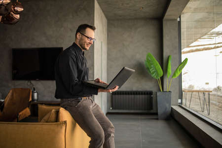 Smiling businessman is sitting in the lobby of the office and working on a laptop. Male business...