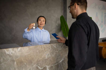 Asian woman receptionist handing over the keys to the room above the counterの写真素材