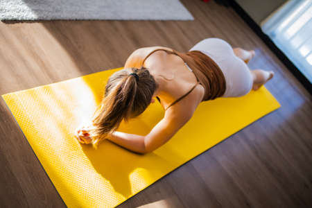 Young slim woman is doing yoga in room filled with light, the girl performs yoga stands and elements near window.の写真素材