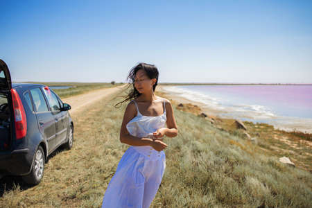 Attractive young asian woman standing on a windy beach of pink sea. road trip by car.