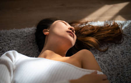sensual young asian woman with closed eyes lying on bed in sun light