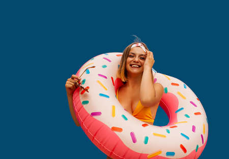 Portrait of a laughing girl dressed in swimsuit holds inflatable ring isolated over blue backgroundの写真素材