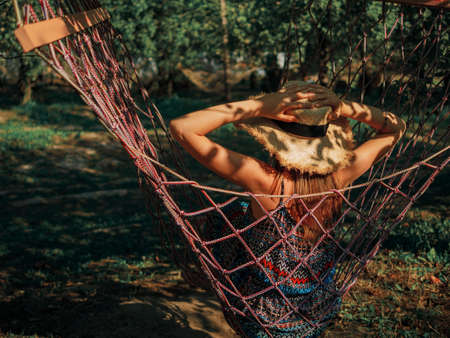 Young relaxed girl in hammock in garden at home at bright sunset. Slow living, gadget detox and weekend leisure activity.の写真素材
