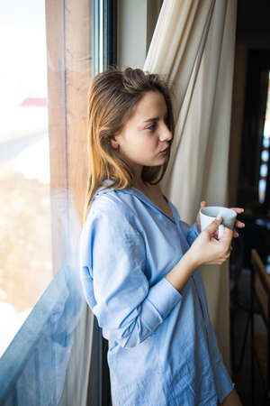Cup of tea or coffee. Woman drinking hot beverage and enjoying morning, sitting on window and dreaming, relaxed mood.の写真素材