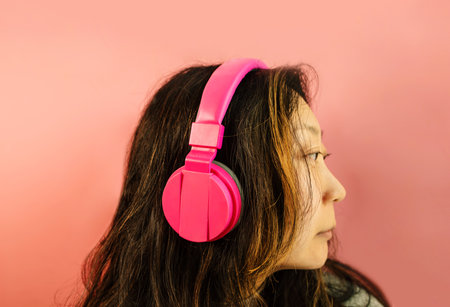 Asian girl enjoy music on headphones. pink background. Youth style, leisure.の写真素材