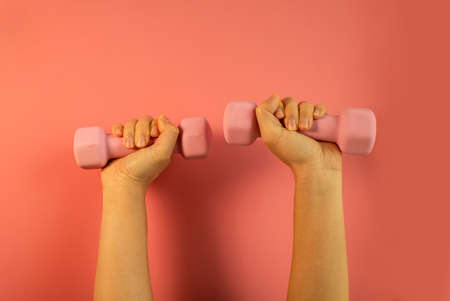 A woman's hand holds a pink dumbbell isolated on a pink background. Equipment for training at home. fitness and activity. The concept of sport and healthy lifestyle.の写真素材