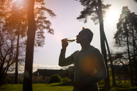 Thirsty athlete drinking water after workout. young sportsman drinking water, having a break during exercising open air, side viewの写真素材