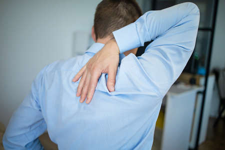 Feeling tired. Back view of frustrated young man looking exhausted and massaging his neck while...