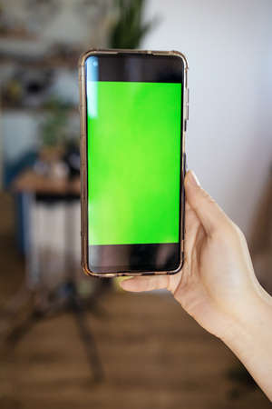 Woman holding a smartphone (green screen) at homeの写真素材