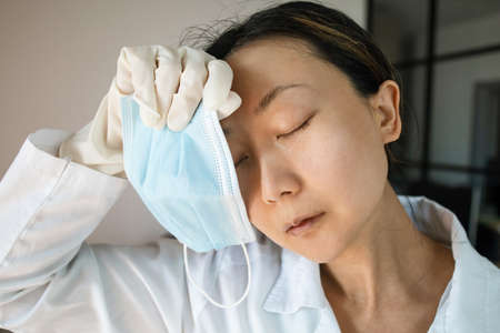 An experienced and tired asian woman doctor in a protective mask, eyes close-up. Protection from...