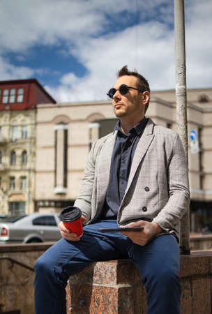 Handsome young man rest with tablet and coffee in city on a spring day.の写真素材