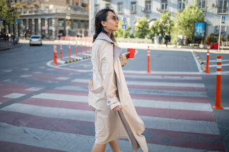 Portrait of a successful happy asian woman in sunglasses on her way to work crossing the street.