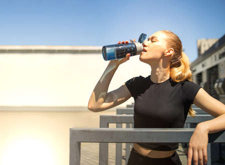 Shot of a beautiful female runner standing outdoors with a bottle of water. Fitness woman takes a...