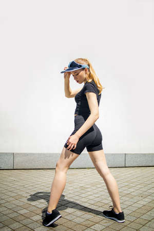 Cute smiling and laughing young blonde woman in a cap, exercising in city outdoor trim trail...
