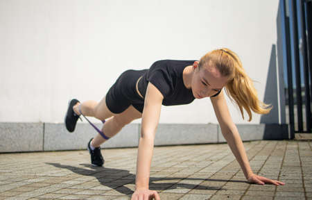 Pretty young fit woman with rubber bands exercise in urban environment.