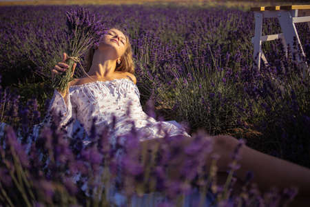 Young beautiful blonde woman lying in lavender field on summer dayの写真素材