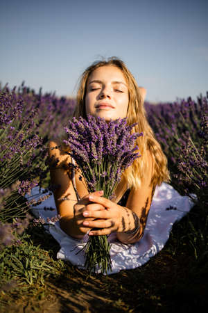 Young beautiful blonde woman lying in lavender field on summer dayの写真素材