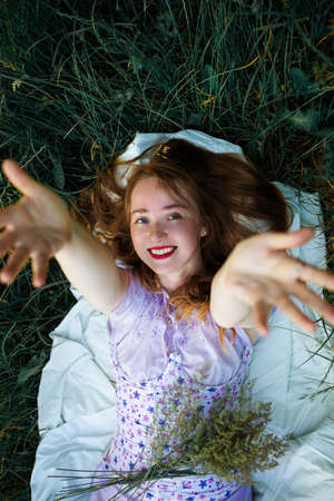 A beautiful girl with long red hair lies on the green grass and smiles.の写真素材