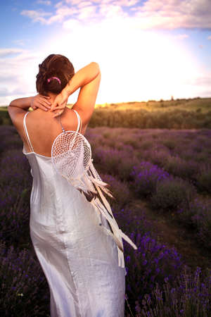 Young pretty asian woman in a white silk dress holding dreamcatcher in lavender field at sunset.の写真素材