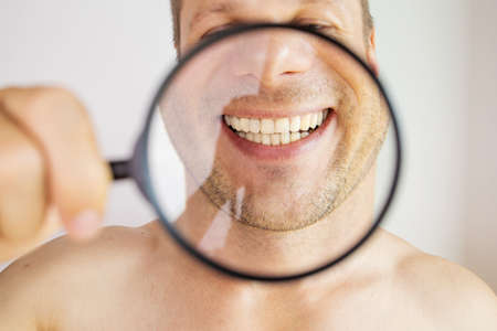 Happy young man smiling, showing his perfect healthy teeth through a magnifying glass close-upの写真素材