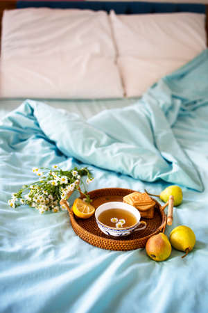 a cup of hot tea with chamomile on a tray in bed. Blue sheets with breakfast in bed.の写真素材