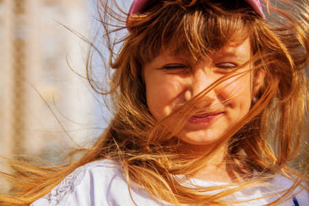 Portrait of child girl with blonde hair blowing in the wind. windy weather concept.の写真素材