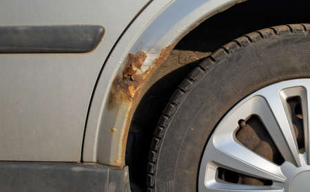 Part of a silver car with rust and a holes in the wing and a black tire with a deep off-road treadの写真素材