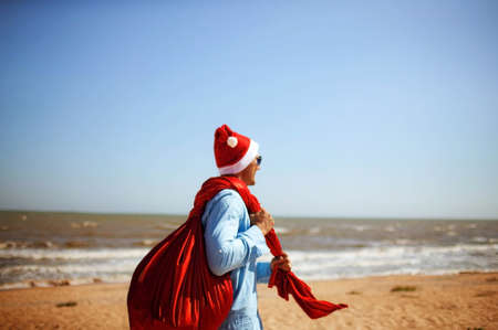 Christmas Santa Claus is running with a big bag full of gifts rush now for kids along ocean tropical sandy beachの写真素材