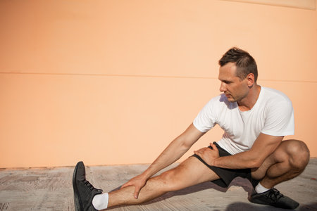 Handsome sports guy exercising fitness outdoors against wall, athletic man doing warm-up, healthy...