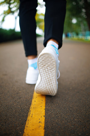 Closeup Runner feet running on the asphalt road behind yellow line.