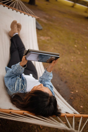 Cheerful portrait of beautiful asian woman enjoy relax lay down on hammock on nature forest woods outdoors park and smiling to tablet - roaming connection and smart working jobの写真素材