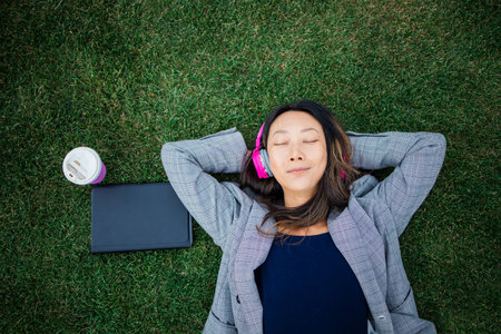 Asian woman relaxing on the grass while listening to music, top view.の写真素材