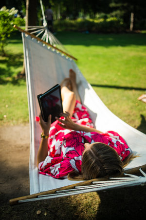 Young blonde woman resting in a comfortable hammock in a green garden on a sunny day.の写真素材