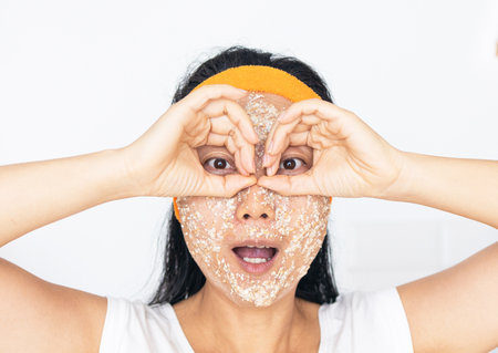 Portrait of a happy Asian woman using natural secrets for skin care (ingredients on the table: oats, flour, eggs, leaves)の写真素材